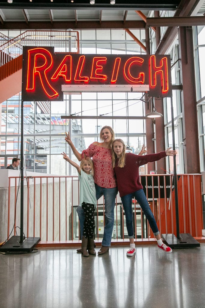 woman and two girls posing under raleigh sign at train station