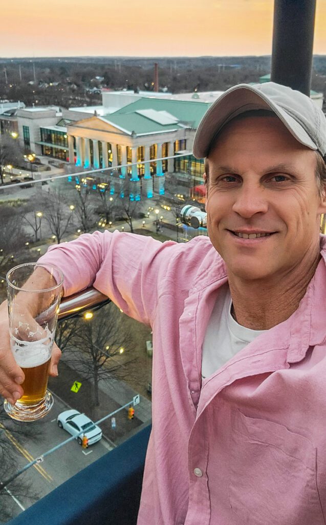 a man smiling at the camera while holding a glass of beer