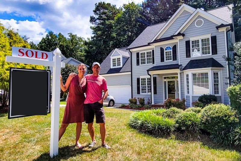 a couple standing in front of a house with a \"sold\" sign
