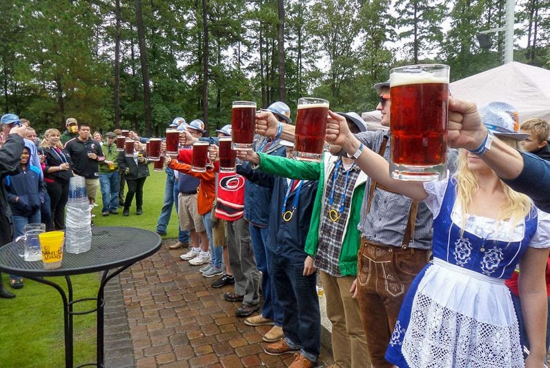 People standing in a line holding up glasses of beer