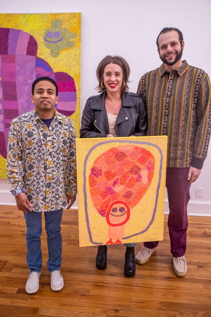 A group of people posing for the camera holding a painting
