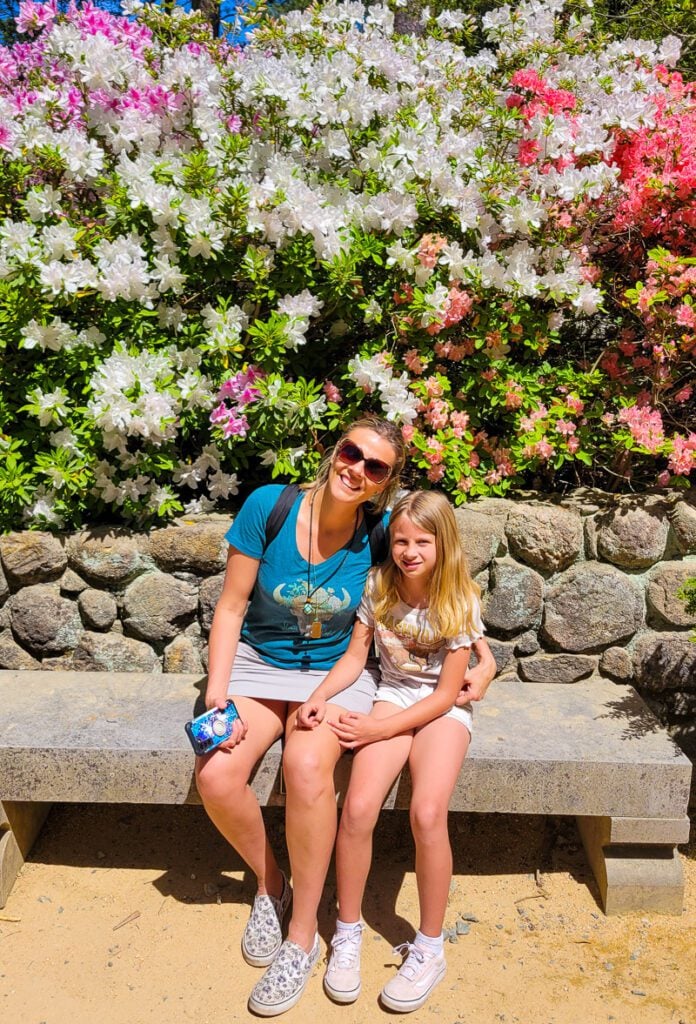 Girls sitting on a bench in front of a flower bush