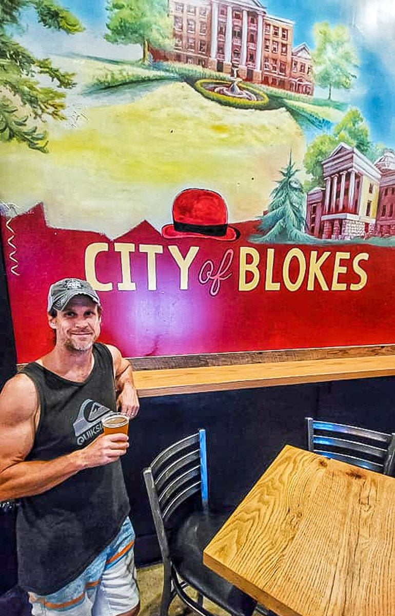 Man holding a beer posing in front of a sign