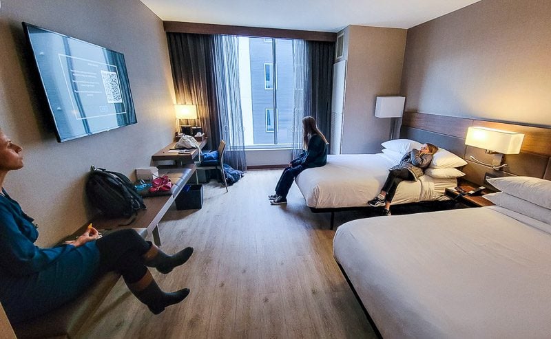 A person in a hotel room with a bed and looking at the camera