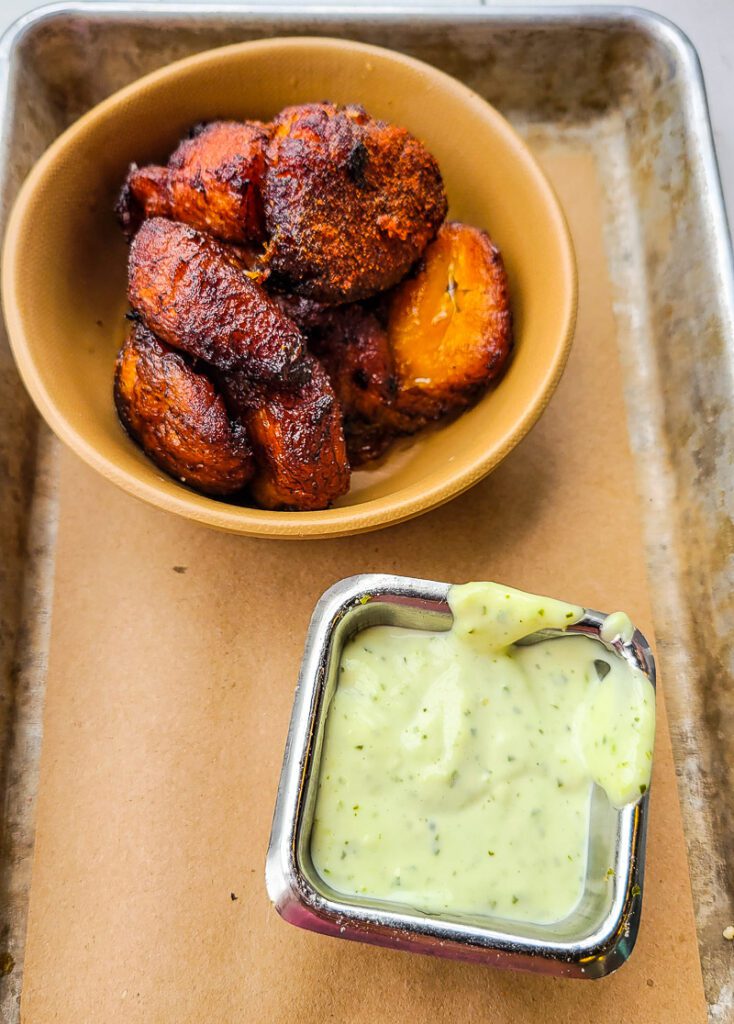 A bowl of plantains with a side of sauce