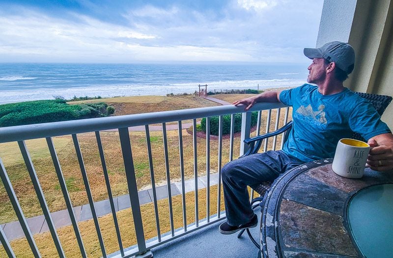 man enjoying coffee on balcony of Grand Villas with views of Indian Beach