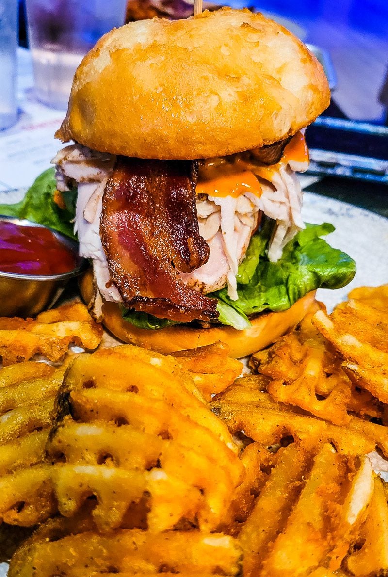 A close up of a burger with bacon and fries on a plate