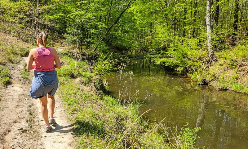 A man standing next to a river, on a hiking trail