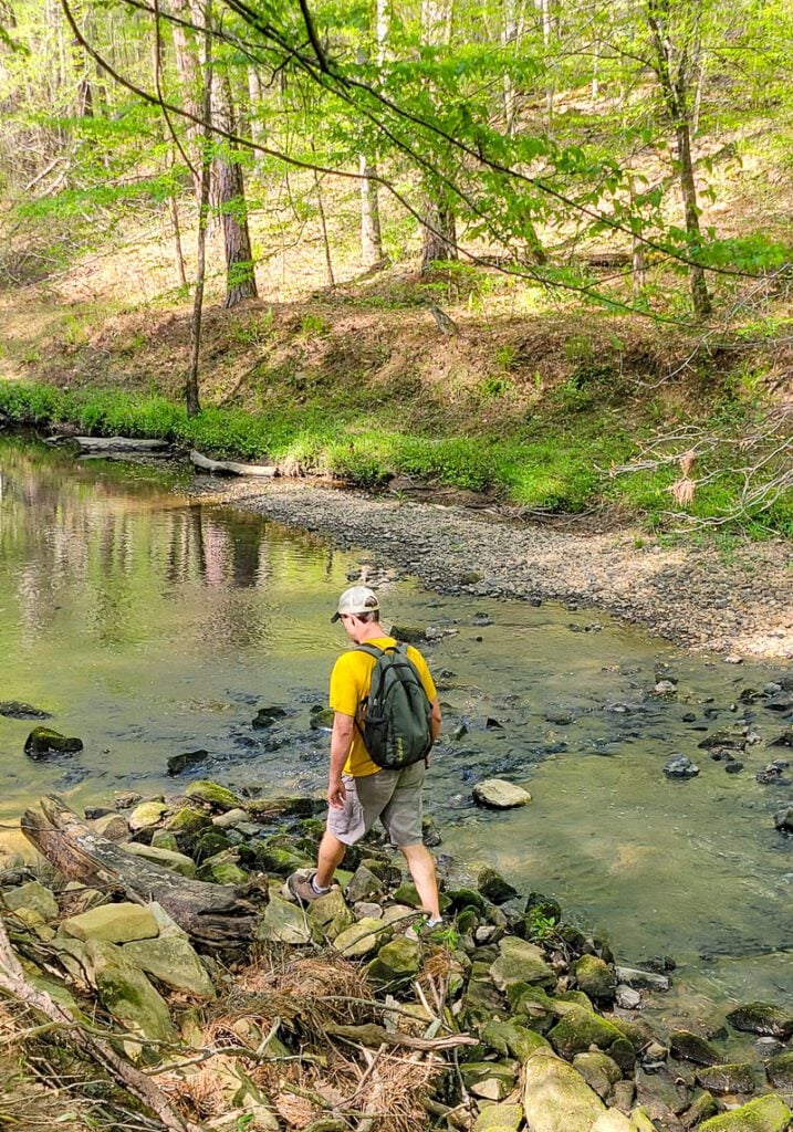 A man standing next to a river, on a hiking trail