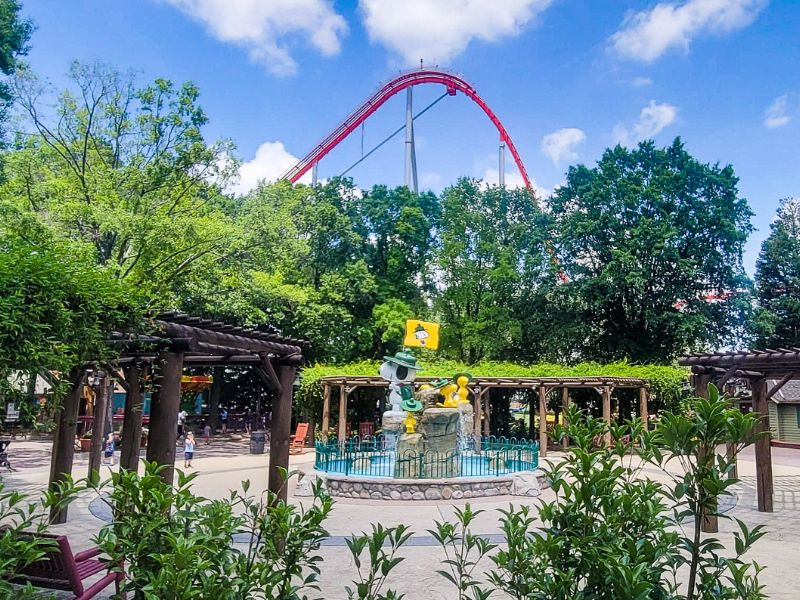 statue of snoopy with a roller coaster and shady trees