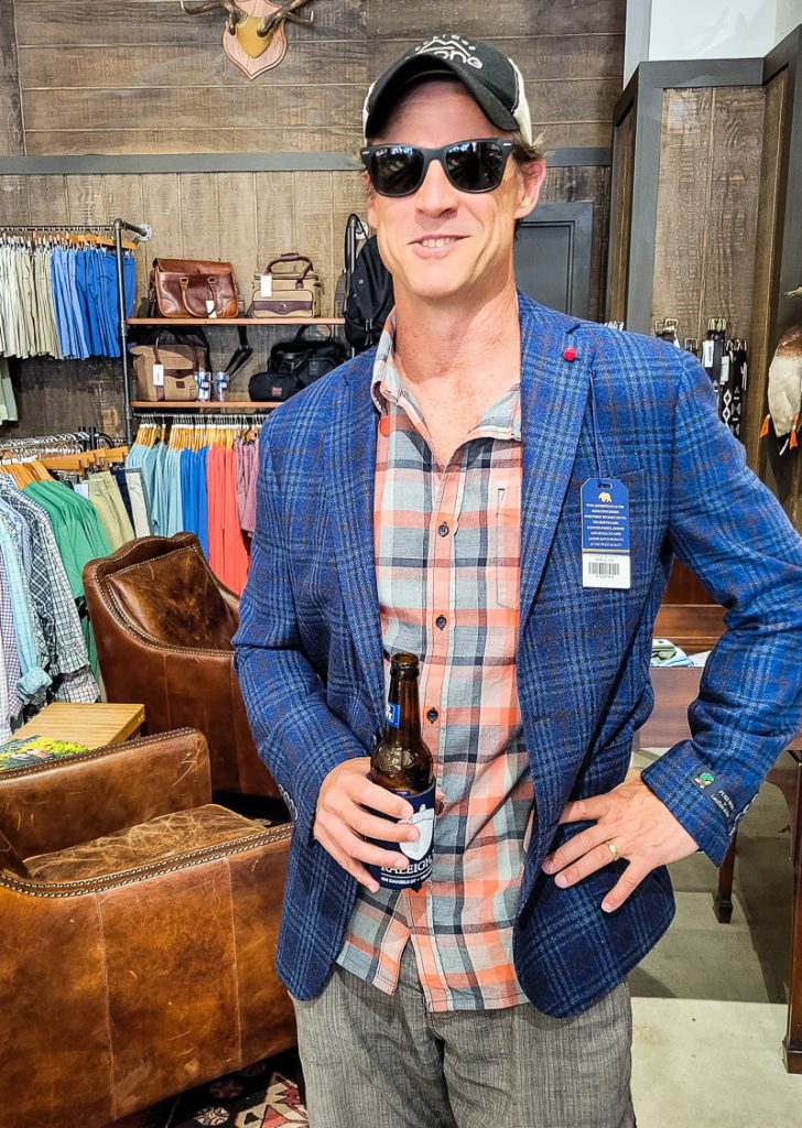 Man holding a beer and trying on a sports coat