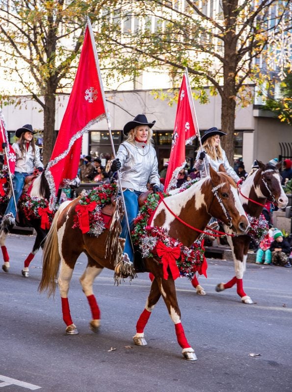 women carrying red flags riding on horses covered in Christmas wreaths