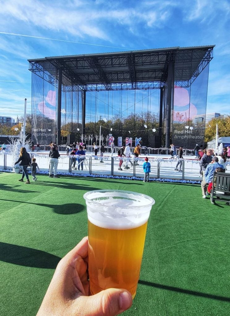 man holding beer with view of the  Raleigh Ice skating Rink