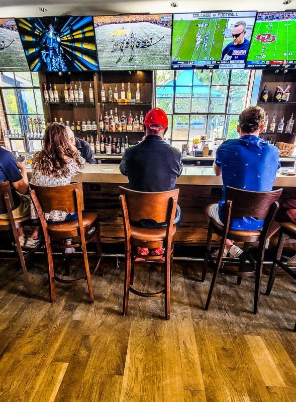 Three people sitting at a bar watching sports