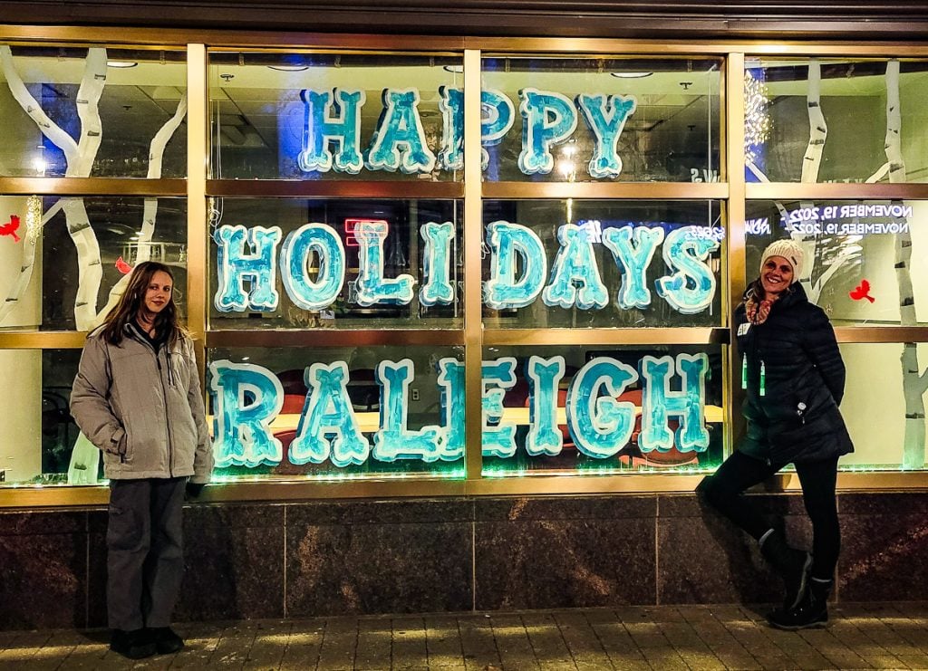 woman and girl standing beside a sign that says happy holidays raleigh painted on the storefront window