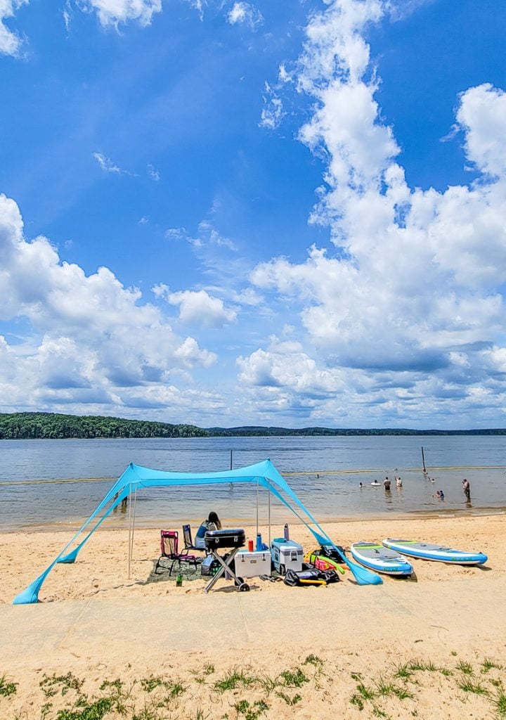 Families sitting under a beach tent and swimming at a lake