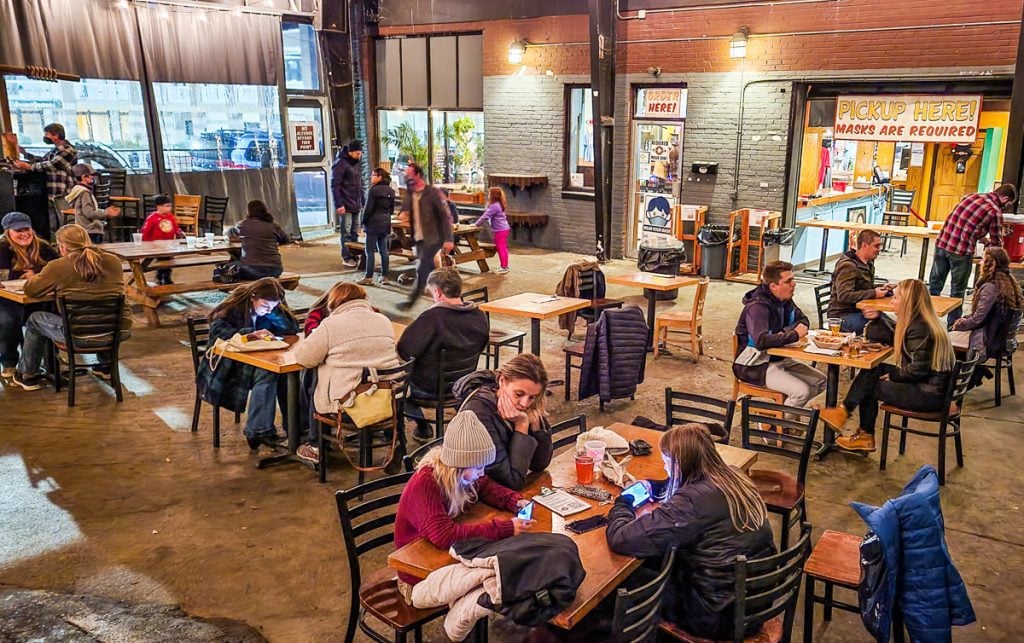 Customers sitting at tables and chairs drinking and eating at a brewery.