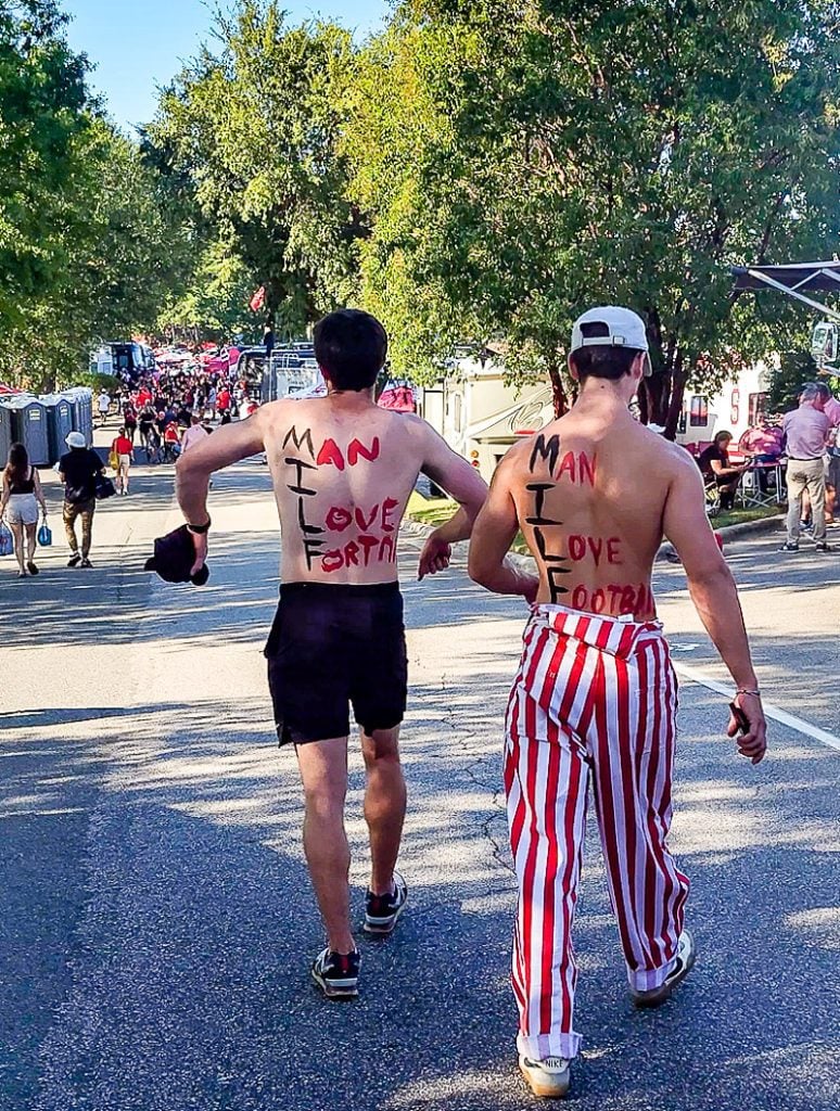 Two guys with their shirts off with words painted on their backs