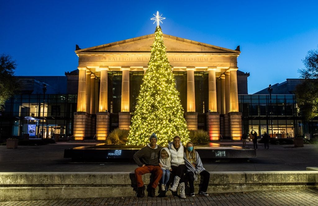 Family getting a photo in front of a Christmas tree and a building