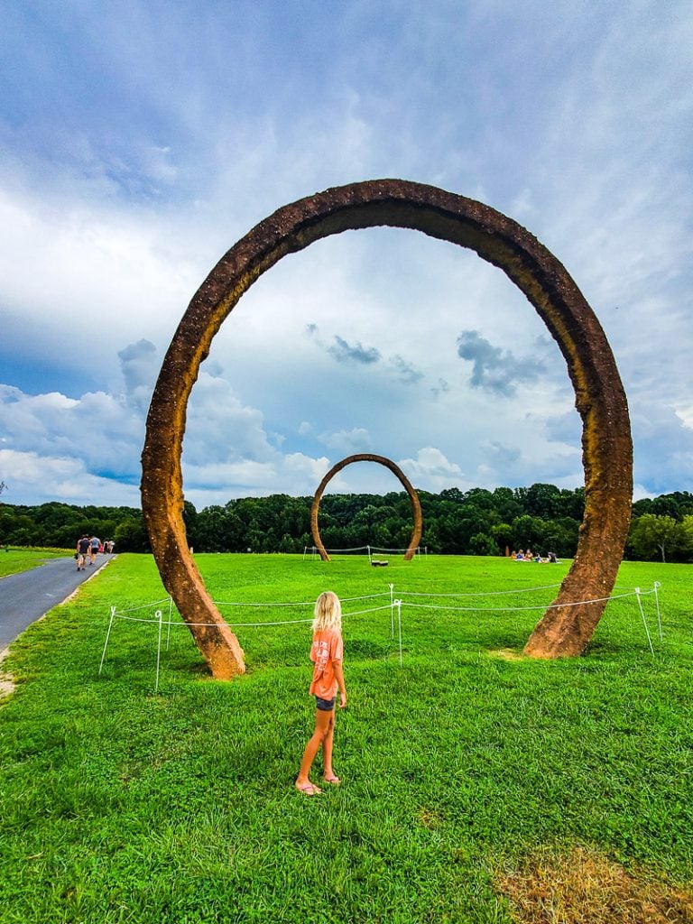 Young girl looking at large steel ring art sculpture
