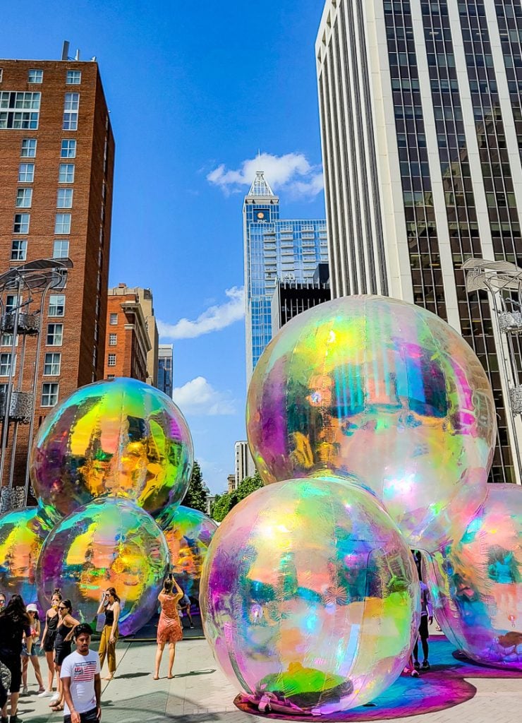 People looking at large colorful balls surrounded by city buildings at an arts festival