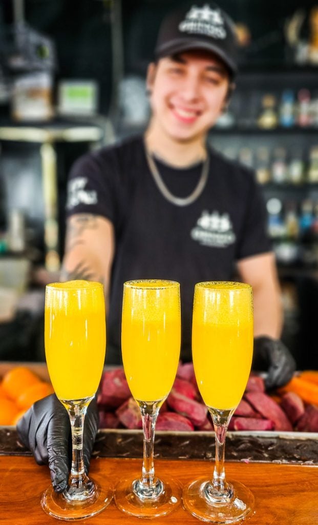 Three glasses of mimosa on a bar with a barman