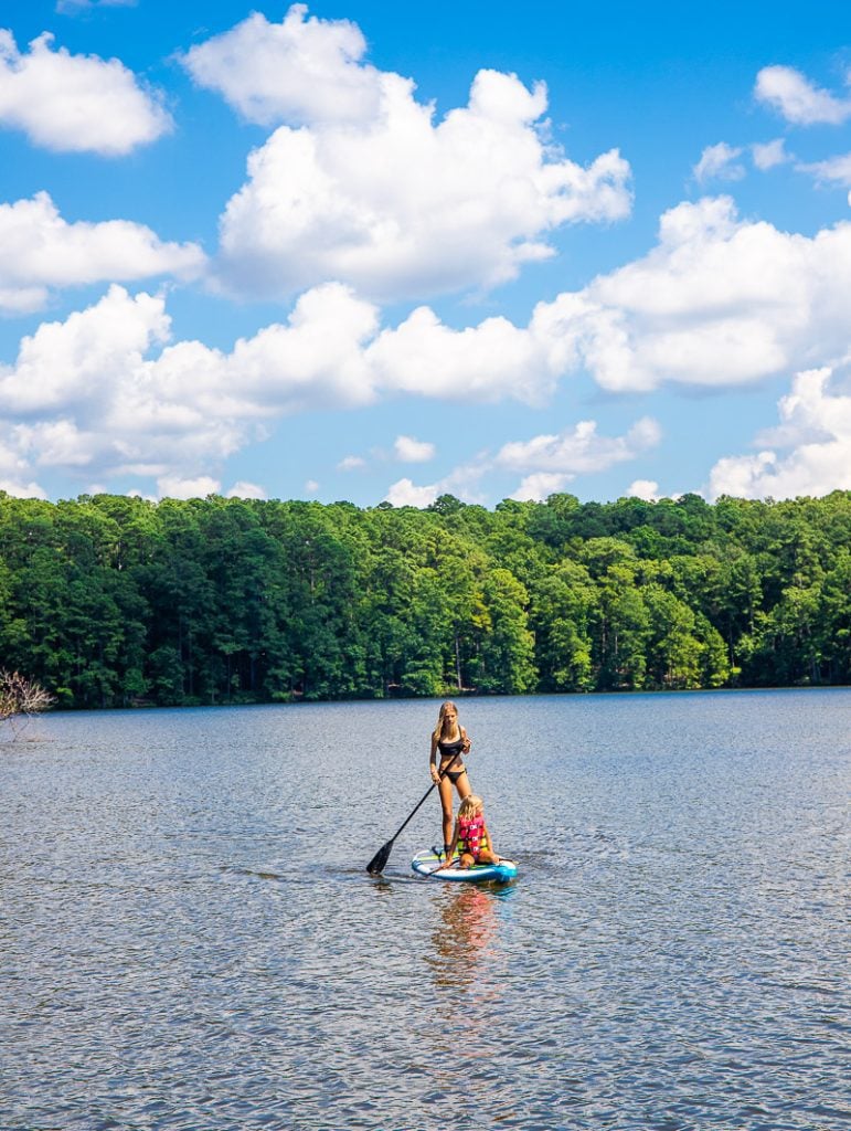 Two sisters paddling on a stand up paddle board on a lake.