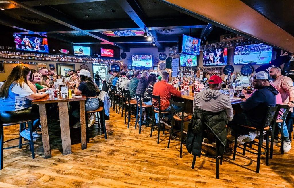Group of people sitting at a bar watching sports on TV