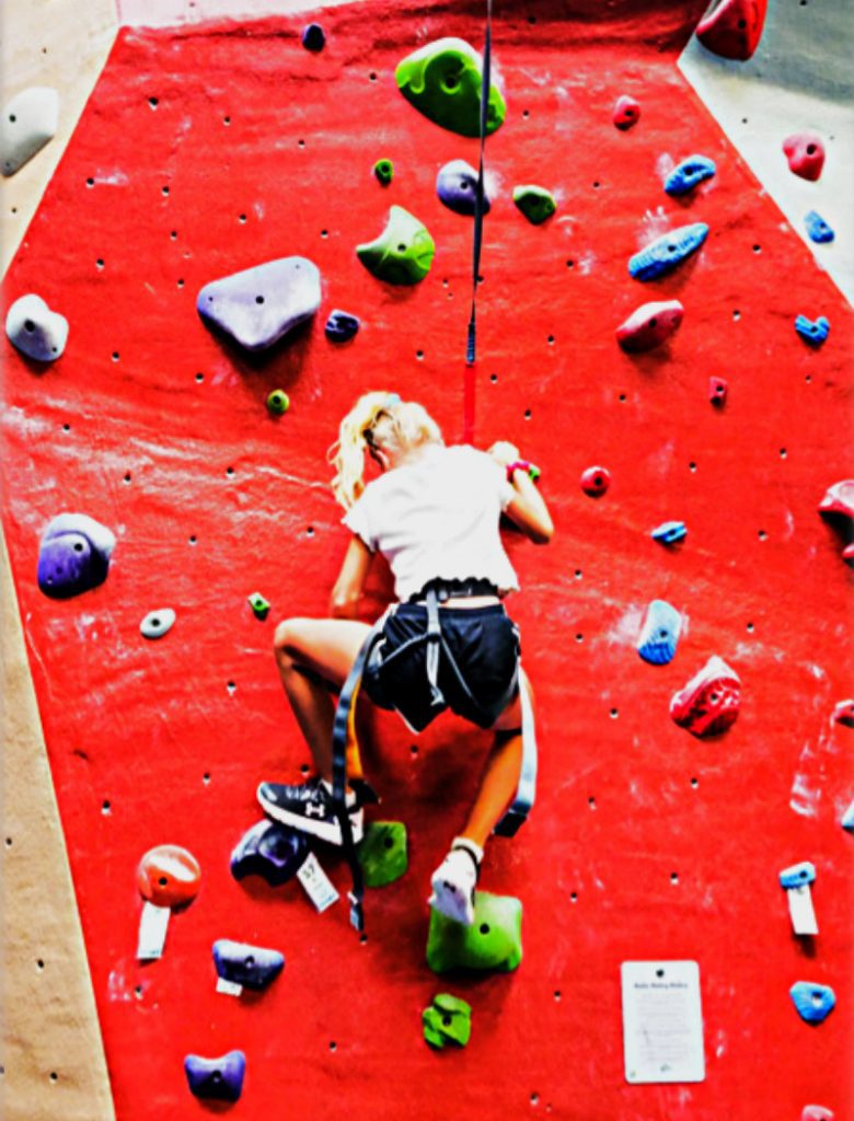 Young girl climbing up a wall at indoor rock climbing.