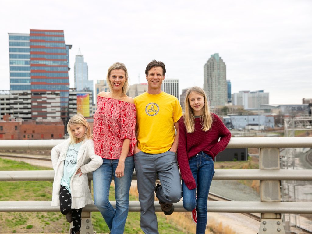 Family of 4 standing on a bridge with buildings in background