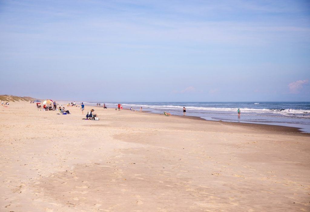 People sitting and walking along a beach.