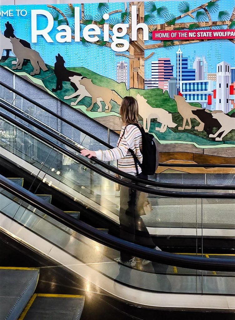 Lady riding an escalator looking at a sign that says Raleigh.