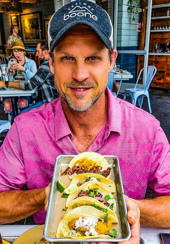 Man holding up a tray of four tacos