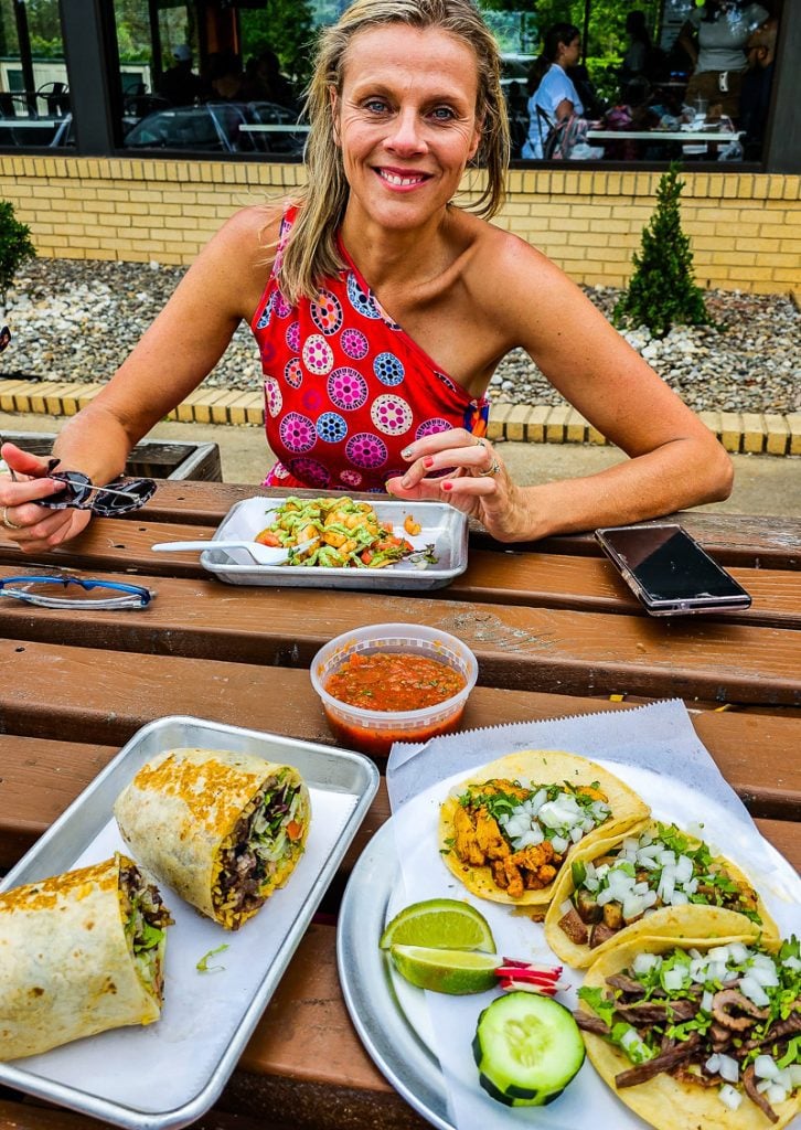 Lady sitting at a table with Mexican food including burrito's and tacos