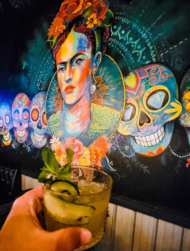 Hand holding a Margarita in front of a mural