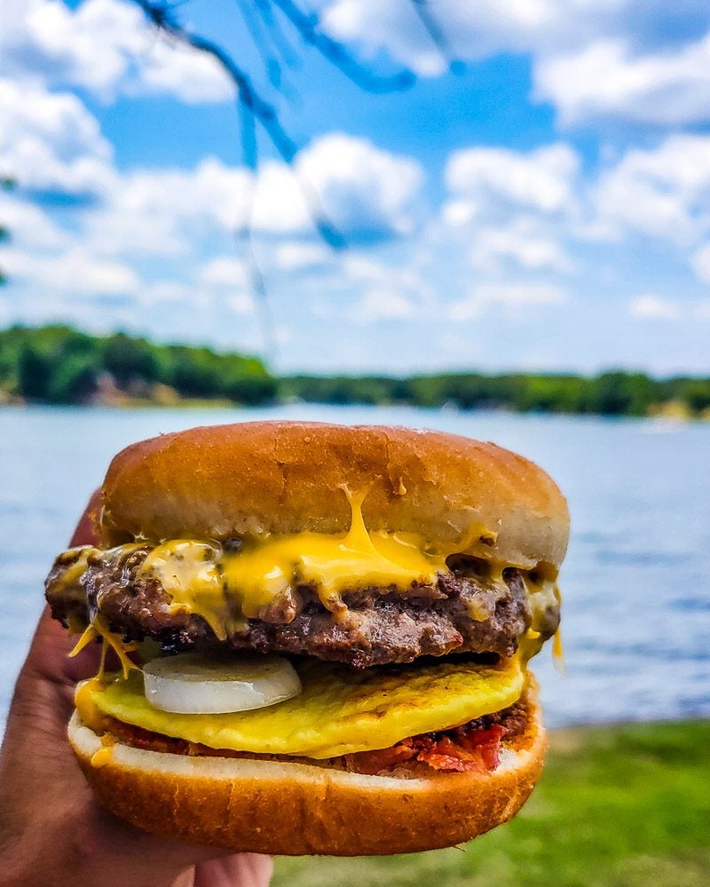 Hold holding up a burger with a lake in the background
