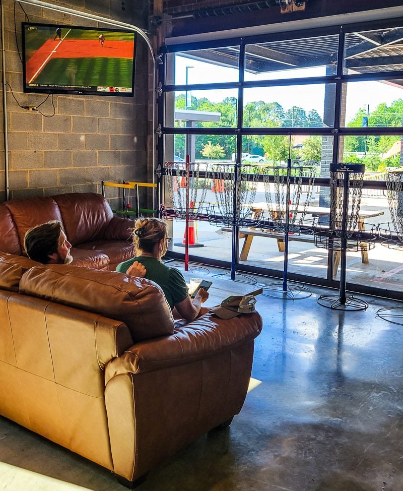 Man and lady sitting on a couch inside a brewery looking out a window