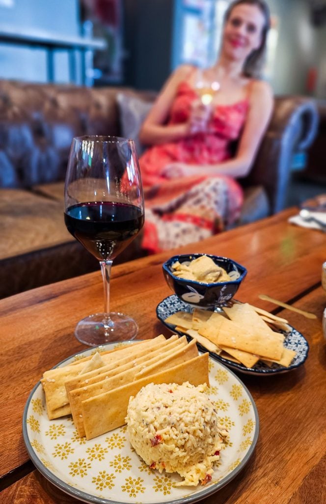 lady sitting on a couch with a glass of wine and plate of cheese and crackers