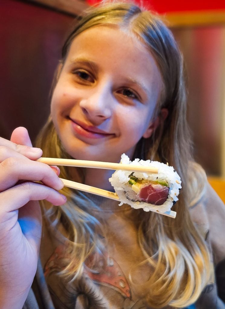 Girl holding chopsticks with sushi at Cowfish in North Hills