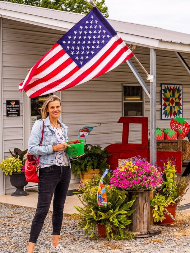 Caroline Makepeace (a woman) holding a bucket of strawberries standing under an American flag