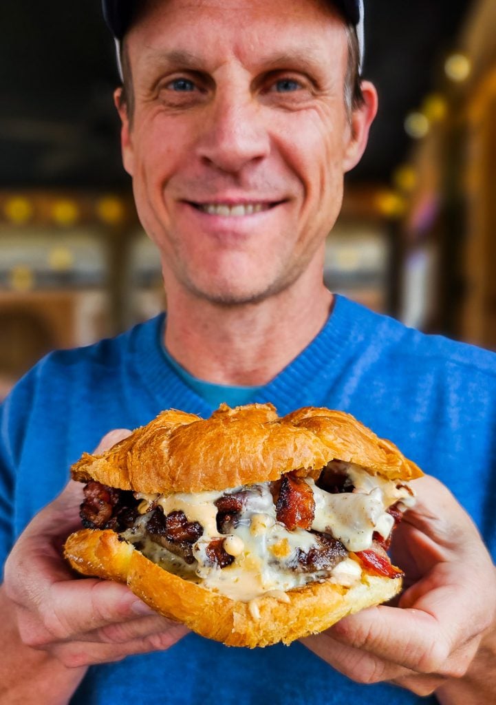 Craig Makepeace holding up a cheeseburger with bacon