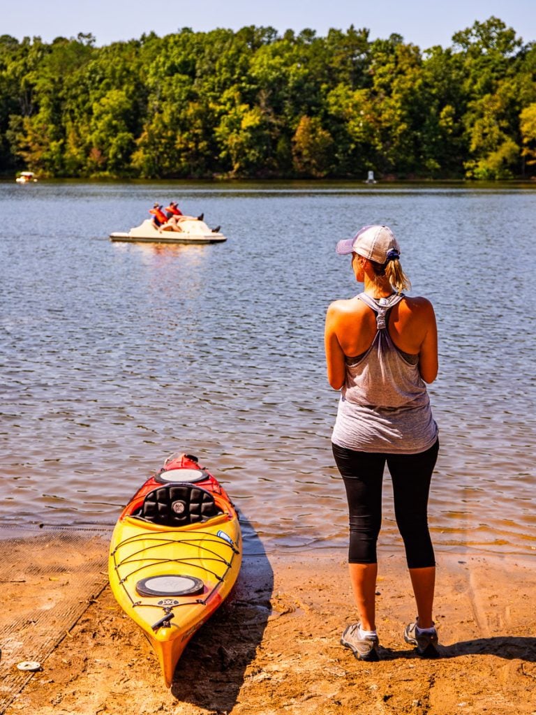 Lady standing at the edge of a lake with a kayak