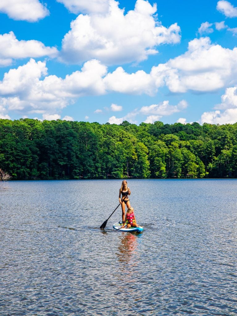 Two young girls on a paddle board on a lake surrounded by forest