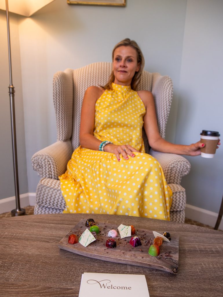 Lady sitting in a chair holding a coffee with chocolates on the table