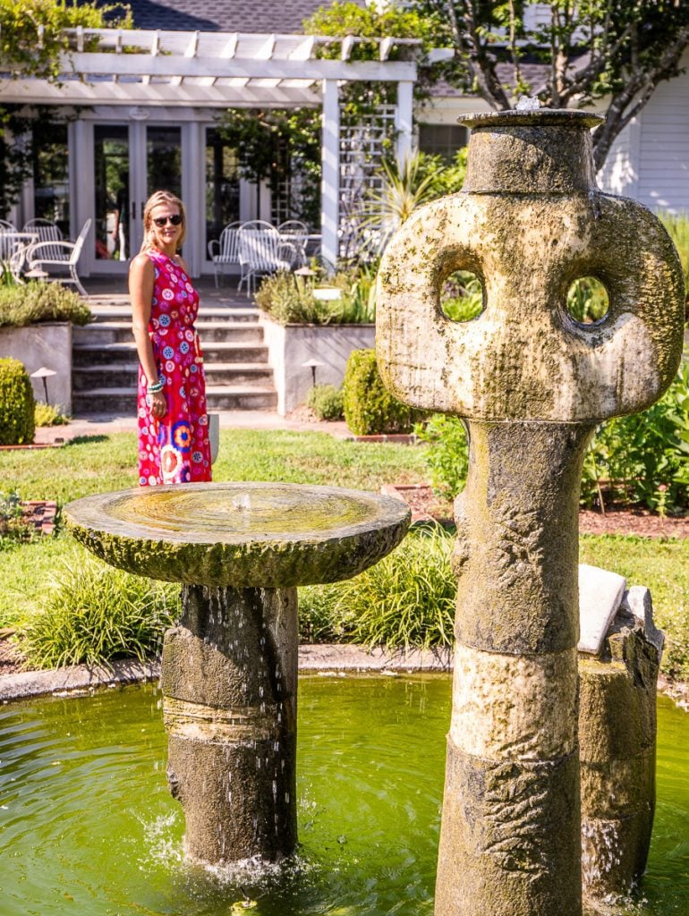 Lady standing behind a water fountain in a garden