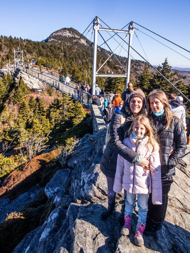 Mom and two daughters standing on a rock ledge with a bridge behind them