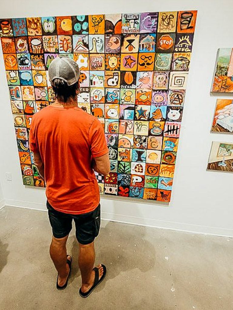 Man in orange shirt looking at art on the wall