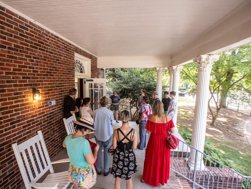 People standing on a porch with white rocking chairs and pillars.