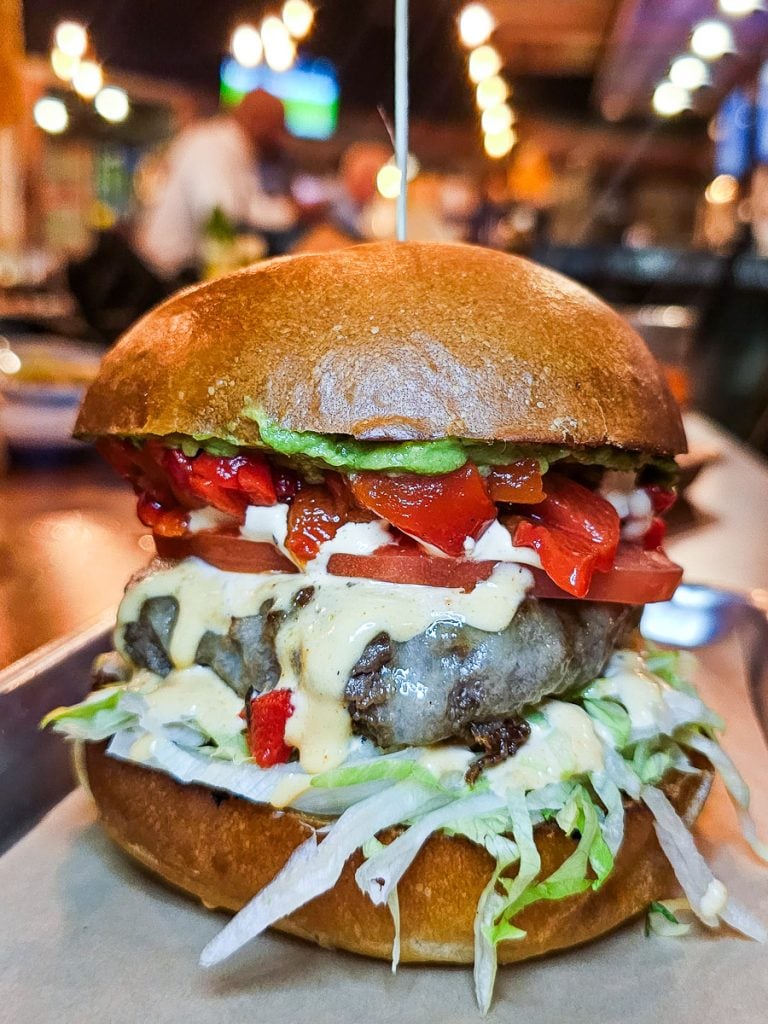 Burger with cheese, red peppers, lettuce and avocado.