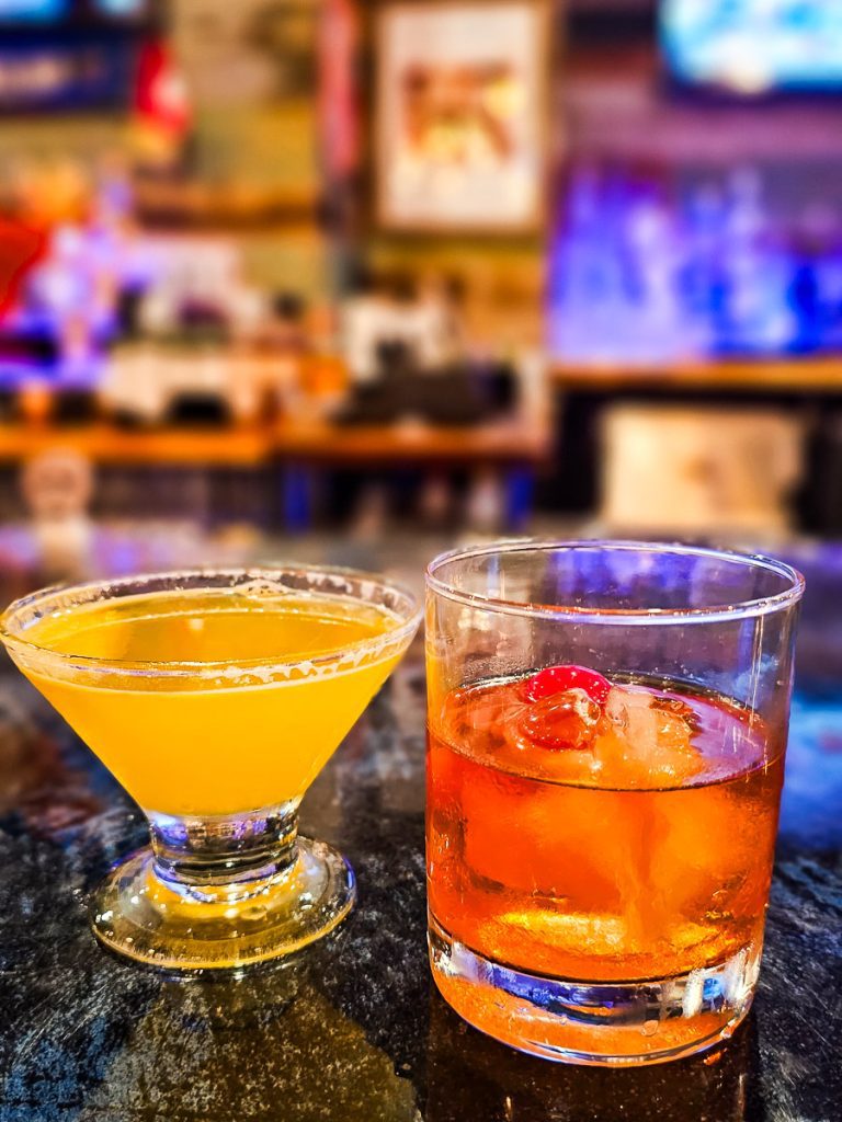 Two cocktail drinks on a bar.